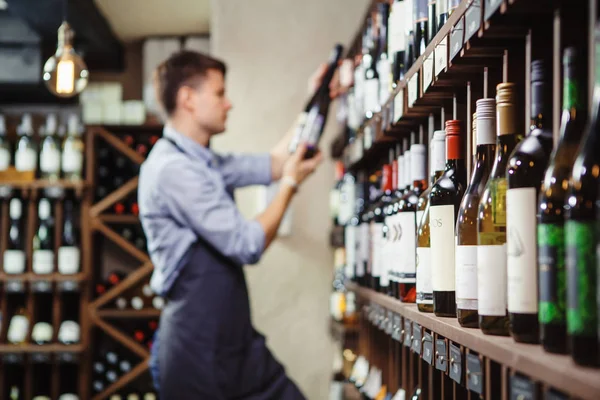 Estantes con vino de élite y desenfocado sommelier joven reflexivo — Foto de Stock