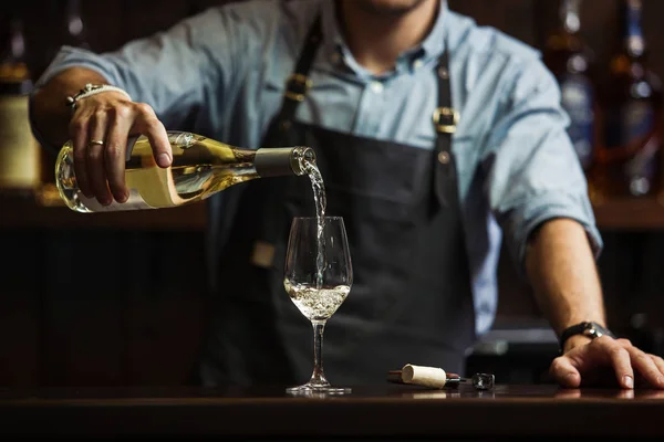 Sommelier masculino vertiendo vino blanco en las gafas de vino de tallo largo . — Foto de Stock