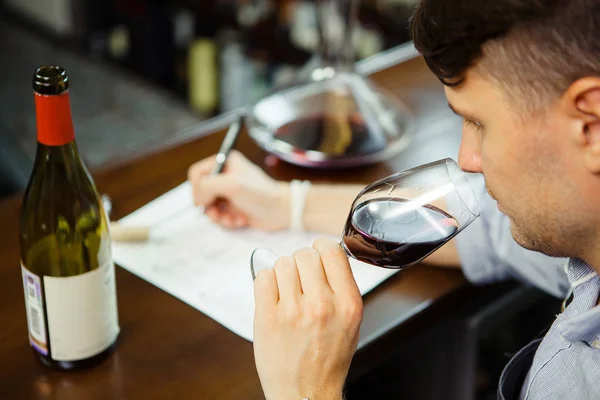 男侍酒师品尝红酒和记笔记的但在酒吧柜台 — 图库照片