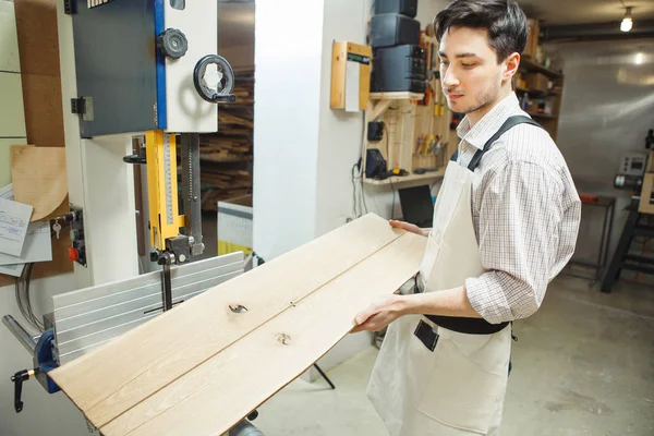 Junger Arbeiter hält zwei Planken in der Hand und betrachtet sie — Stockfoto