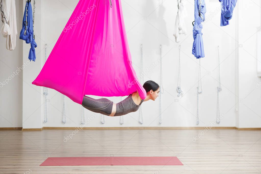 Adult woman practices anti-gravity yoga position in gym.