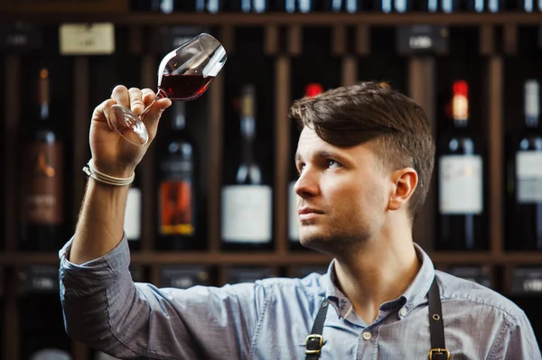 Arka planda bir şişe kırmızı şarap, erkek şarap garsonu içkinin değerini biliyor.