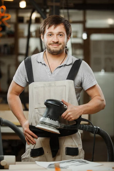 Lachende timmerman stand met Excentrische schuurmachine in handen — Stockfoto