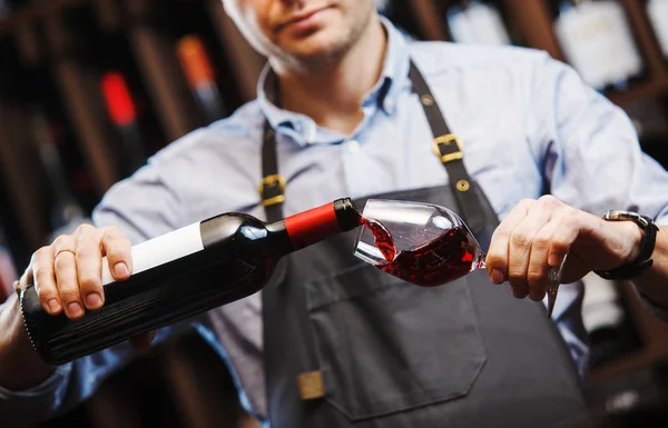 Samec sommelier nalévá červené víno do dlouhých vinných sklenic. — Stock fotografie