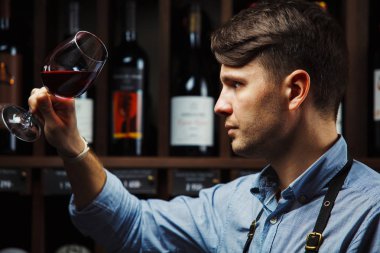 Arka planda bir şişe kırmızı şarap, erkek şarap garsonu içkinin değerini biliyor.