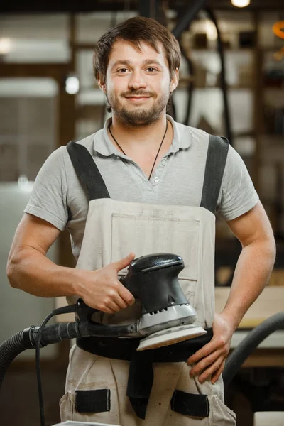 Lachende timmerman stand met Excentrische schuurmachine in handen — Stockfoto