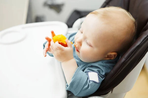 Dziecko siedzi w krzesełko do karmienia i zjada brzoskwinia — Zdjęcie stockowe