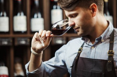 Arka planda bir şişe kırmızı şarap, erkek şarap garsonu içkinin değerini biliyor.
