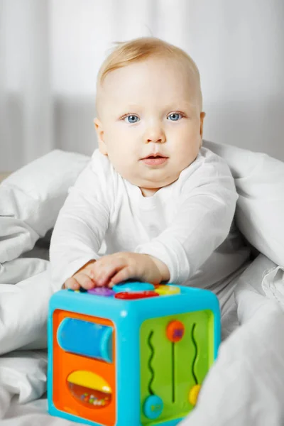 Bebê bonito senta-se em ruim sob cobertor com brinquedo — Fotografia de Stock