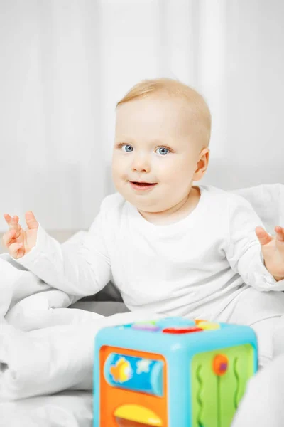 Adorável brincalhão bebê senta-se na cama com brinquedo cúbico — Fotografia de Stock