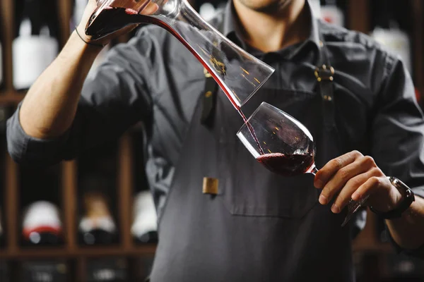 Μπάρμαν χύνει κόκκινο κρασί σε ποτήρι από μεγάλο διαφανές δοχείο — Φωτογραφία Αρχείου