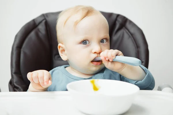 Adorable baby sits in high chair and eats cream soup