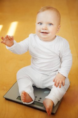 Yüz ifadesi gülümseyen güzel bebek ölçekler üzerinde oturur