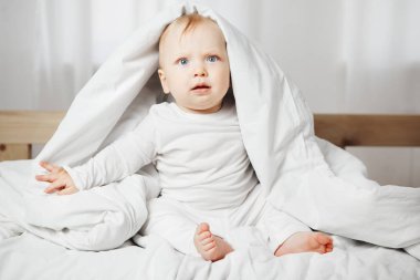 Şirin Bebek şaşkın bakışla geniş yatakta oturur