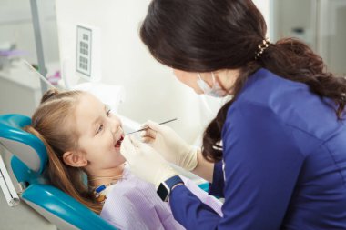 Çocuk diş hekimi sandalyede oturuyor ve yordam gider