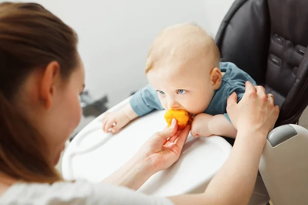 Ребенок в детском стульчике и мама кормит его персиком — стоковое фото