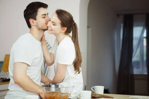 Homem com olhos fechados ternamente beija mulher na bochecha na cozinha — Fotografia de Stock