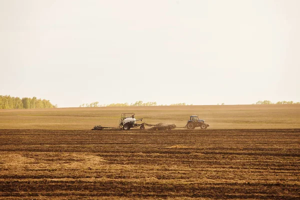 Un trattore con un campo di aratura rimorchio per la semina di macchine agricole si prepara per una nuova coltura . — Foto Stock