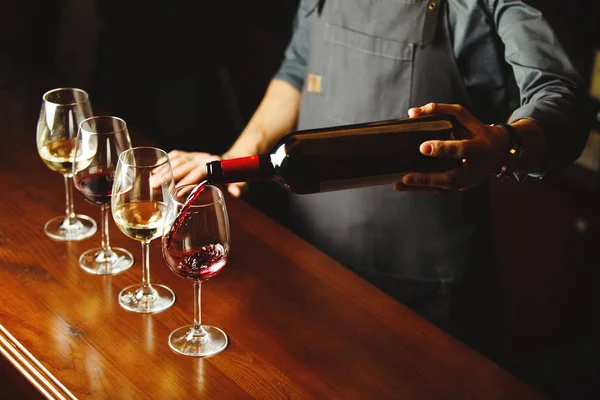 Barman nalévá červené víno ve sklenicích na dřevěnou barovou linku — Stock fotografie