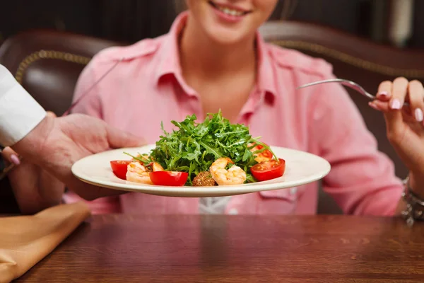 Waiter serve salad with green arugula leaves, tomato and shrimps