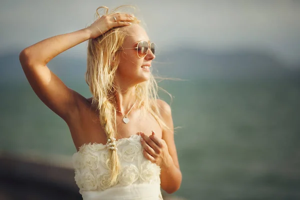 Donna con occhiali da sole e abito da sposa bianco sullo sfondo del mare . — Foto Stock