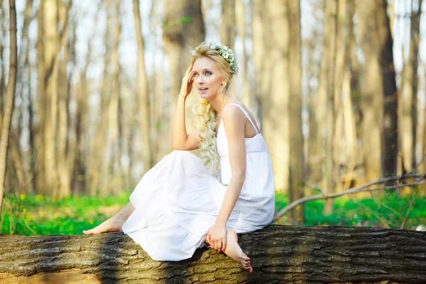 Hermosa mujer en vestido blanco se sienta junto al bosque verde del árbol . — Foto de Stock