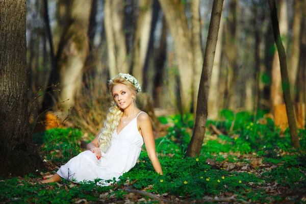 Красива жінка в білій сукні сидить на траві в середині літнього лісу . — стокове фото