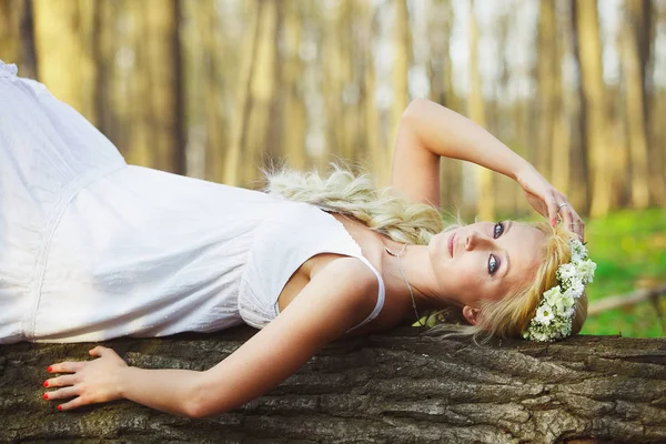 Mulher loira em vestido branco deitado na árvore no meio da floresta . — Fotografia de Stock