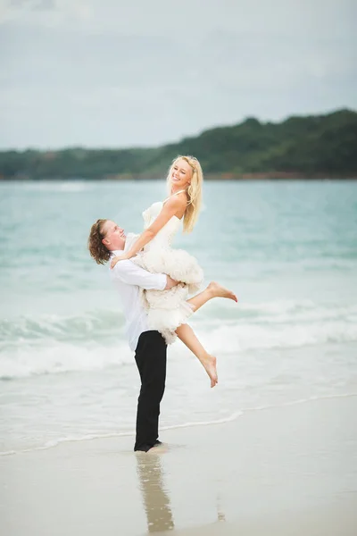 Γαμπρός σήκωσε τη νύφη του από θάλασσα. ευτυχισμένος νεόνυμφους σε μια ερημική παραλία. — Φωτογραφία Αρχείου