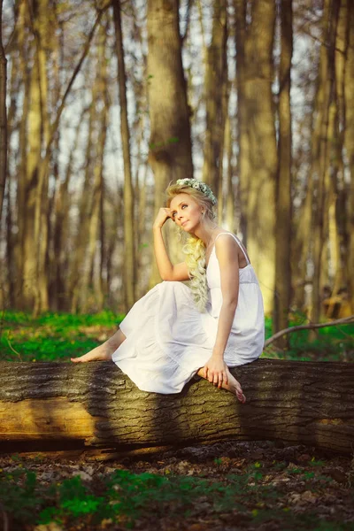 Bela mulher em vestido branco senta-se por árvore floresta verde . — Fotografia de Stock