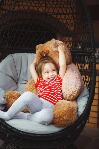 Menina sentada na cadeira no terraço com urso de brinquedo . — Fotografia de Stock