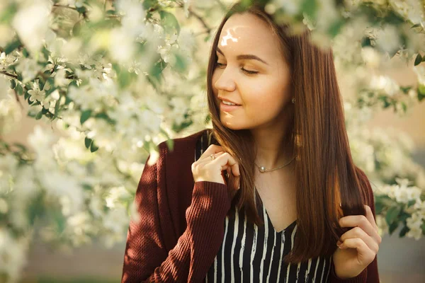 Mujer joven con la piel limpia cerca de un manzano en flor. retrato de niña en el parque de primavera . — Foto de Stock