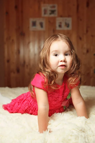 Rödhårig flicka i en rosa klänning som sitter på sängen. — Stockfoto