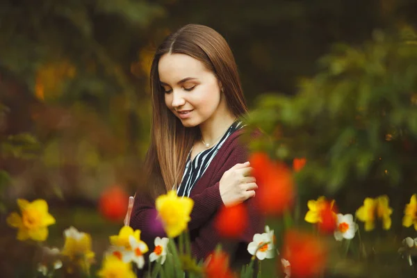 Schönes Mädchen sitzt an den gepflanzten Blumen. — Stockfoto