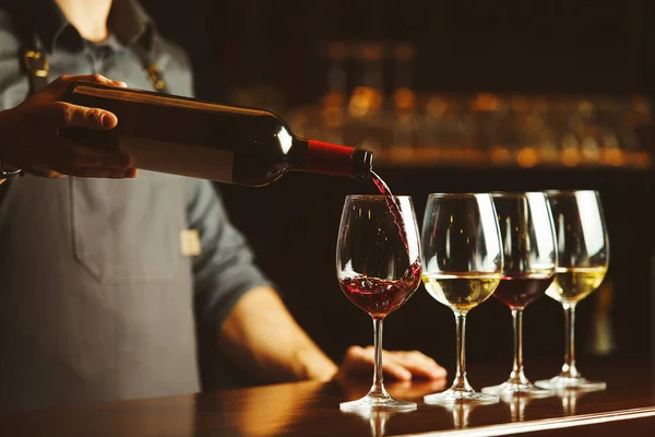 Barman nalewa czerwone wino do szklanek na drewnianej blacie. — Zdjęcie stockowe