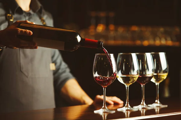 Barmen kırmızı şarabı bardaklara doldurur.
