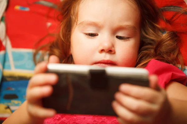 Dívka se pozorně dívá na telefon. nebezpečí přístroj pro dětské vidění. — Stock fotografie