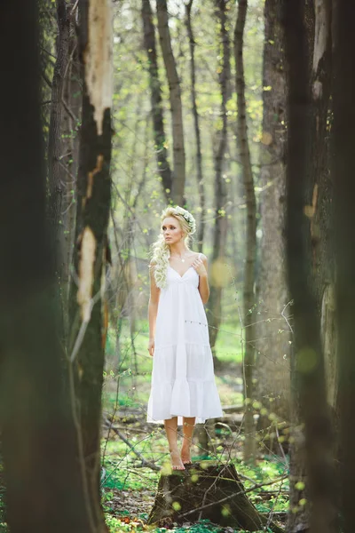 Jovem mulher com cabelo loiro na floresta vestido branco entre as árvores . — Fotografia de Stock