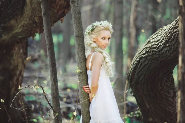 Jovem mulher com cabelo loiro na floresta vestido branco entre as árvores . — Fotografia de Stock