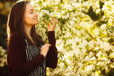 genç kadın çiçek açması ağaca kokluyor. Bahar parkta güzel kız.