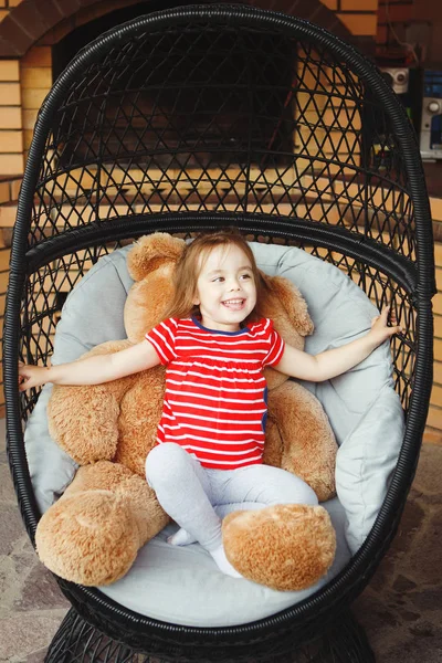 Menina sentada na cadeira no terraço com urso de brinquedo . — Fotografia de Stock