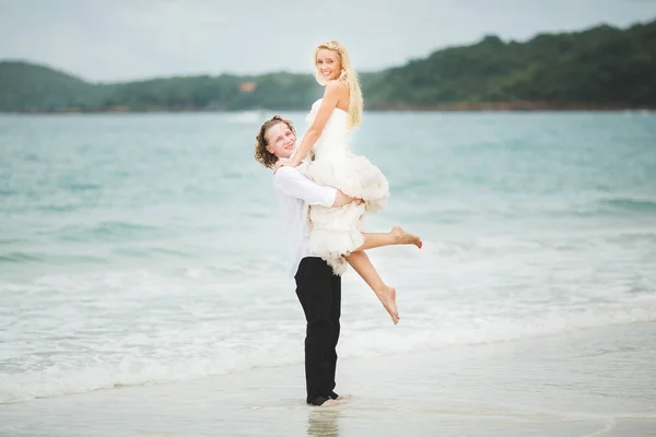 Novio levantó a su novia del mar. recién casados felices en una playa desierta . —  Fotos de Stock