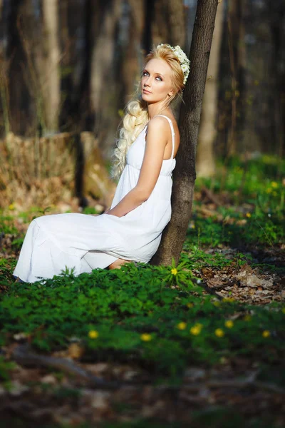 Schöne Frau im weißen Kleid sitzt am Baum grünen Wald. — Stockfoto