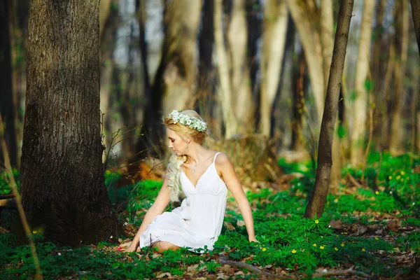 Schöne Frau in weißem Kleid sitzt auf Gras inmitten eines Sommerwaldes. — Stockfoto