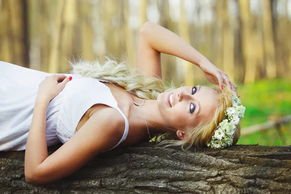 Mulher loira em vestido branco deitado na árvore no meio da floresta . — Fotografia de Stock