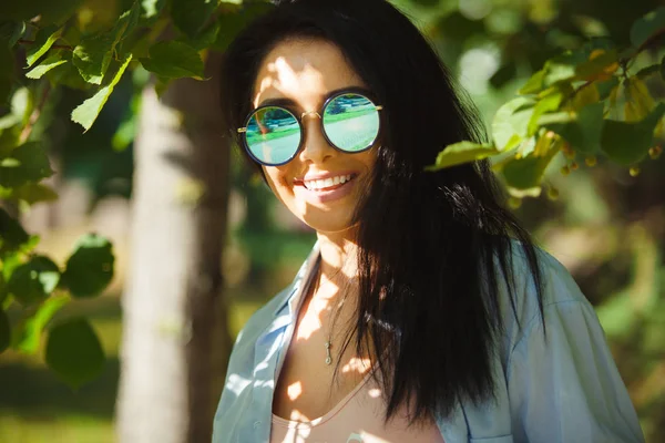 smiling woman wears circular sunglasses.