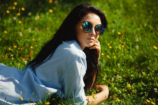 Retrato de mulher encantadora em óculos de sol deitado na grama . — Fotografia de Stock
