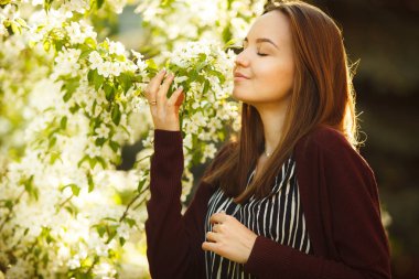 genç kadın çiçek açması ağaca kokluyor. Bahar parkta güzel kız.