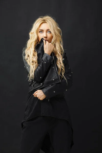 Portret van een meisje met blond haar in modieuze en stijlvolle kleding heeft betrekking op haar gezicht met een lederen jas. — Stockfoto