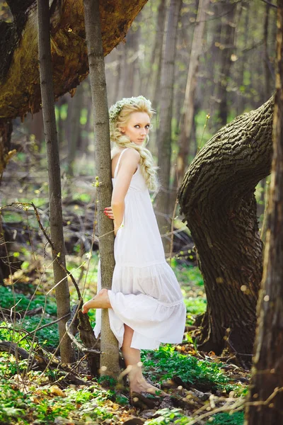 Jovem mulher com cabelo loiro na floresta vestido branco entre as árvores . — Fotografia de Stock